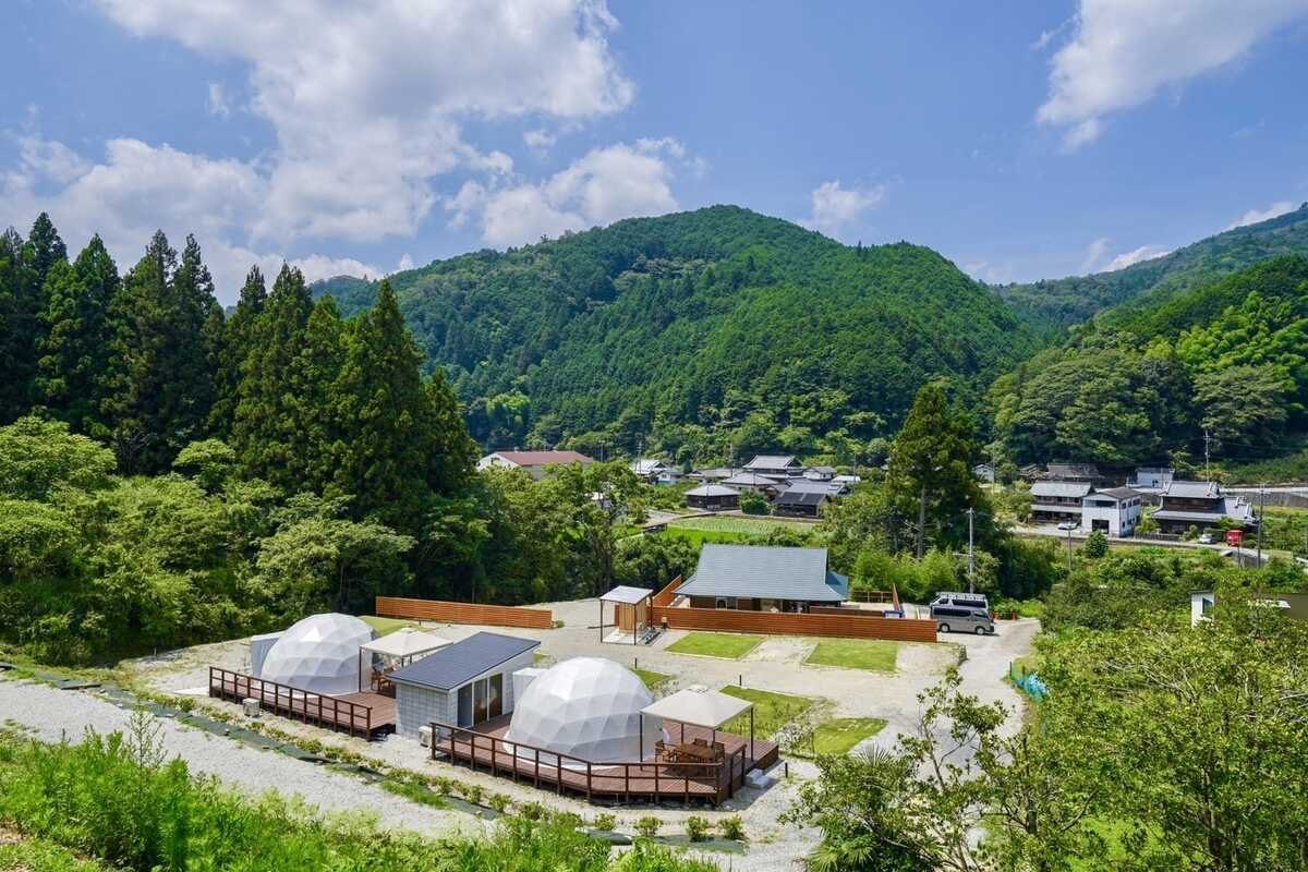 山に囲まれた芝生の向こうに、白いドームテントが並ぶソラニワグランピング