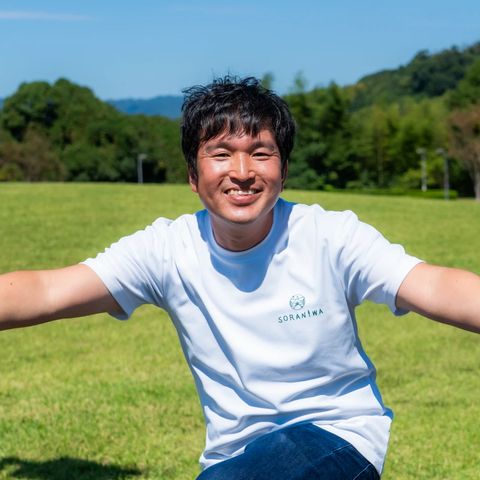 芝生で両手を広げて笑う福井大樹